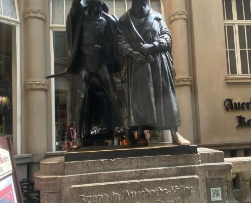 Die Skulptur zeigt eine Szene aus Goethes Faust: Mephisto verzaubert die Studenten Die Skulptur zeigt eine Szene aus Goethes Faust: Mephisto verzaubert die Studenten