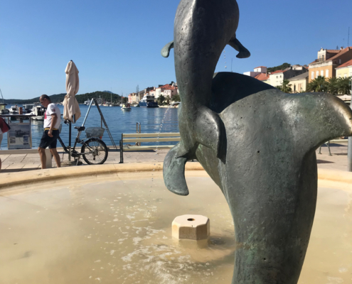Der Delphinbrunnen von Mali Lošinj Die beiden spielenden Delfine stammen vom Bildhauer Vinko Matković aus Rijeka. Der Brunnen wurde 1960 errichtet und erinnert an die Fertigstellung der Wasserversorgung, durch die Mali Lošinj erstmals mit fließendem Trinkwasser aus dem Vrana-See versorgt wurde. Die dargestellten Großen Tümmler sind bis heute charakteristisch für die Gewässer rund um Lošinj.