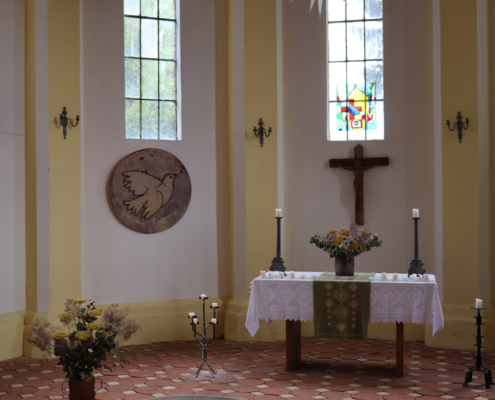 Der schlichte Altarraum der St.-Johannis-Kirche in Boek. Der ursprüngliche Altar ist nicht mehr erhalten; heute prägt ein schlichtes Kruzifix an der Chorwand den Raum. Die helle Gestaltung und die farbig verglasten Fenster geben der Kirche ihre freundliche, ruhige Atmosphäre.