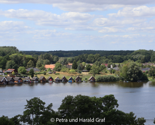 Am gegenüberliegenden Ufer reihen sich kleine Bootshäuser direkt am Wasser. Von oben sieht man erst richtig, wie eng Stadt, See und Natur hier miteinander verbunden sind.